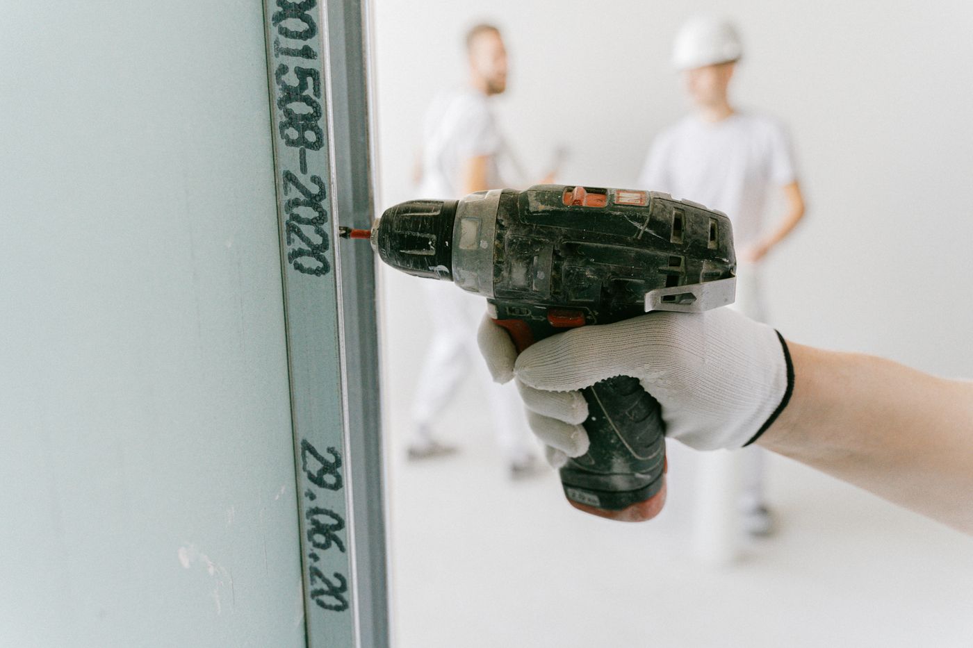 Installer fixing off a wall with a drill, crew working behind on the same floor